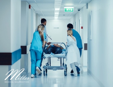 Medical staff pushing person on gurney down hallway
